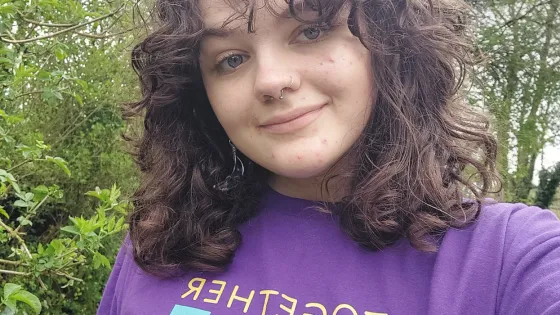 A young woman smiles in a selfie while wearing a 'together we create possible' Young Epilepsy t-shirt.
