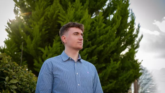 A young man in a blue shirt looks beyond the camera.