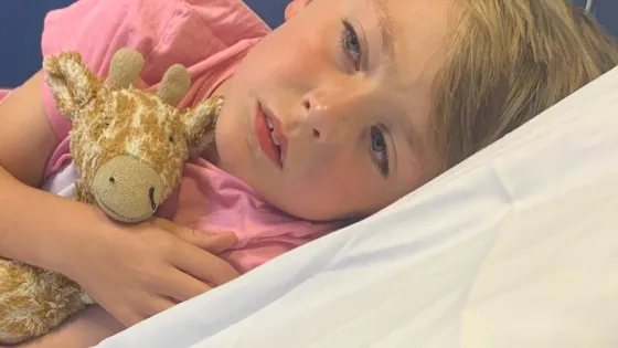 young boy lying on a hospital bed cuddling a giraffe