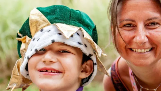 Young boy wearing a green velvet crown sat next to an adult woman. Both are smiling towards the viewer.