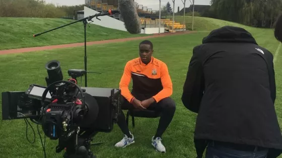 A young man sits before film cameras on a football pitch for a Christmas appeal.