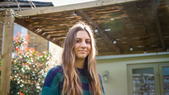 A young woman photographed outside a house smiles slightly to camera.