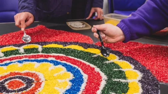 Two individuals spoon colourful stones onto a mural for the SHINE strategy.