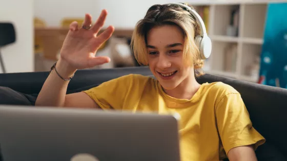 Young boy wearing headphones, waving and smiling on a video call
