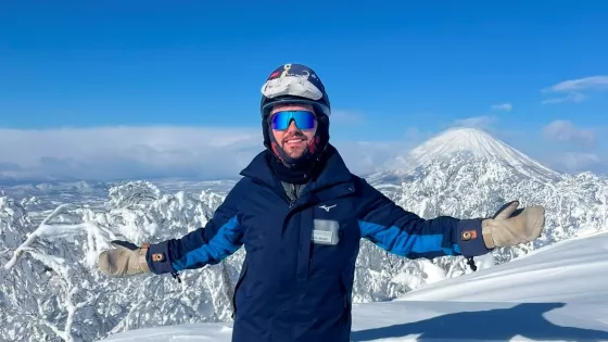 A young man, Miles, stands in snowboarding gear on top of a snowy mountain.