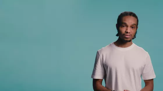 A young man wearing a light t-shirt against a blue backdrop