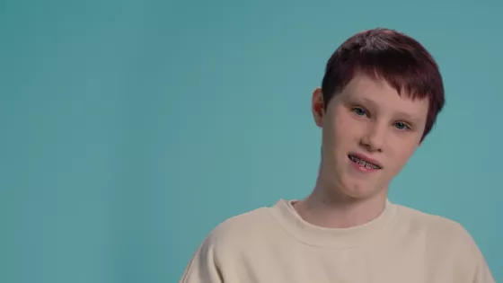 A young Caucasian boy smiles against a blue backdrop wearing a white t-shirt