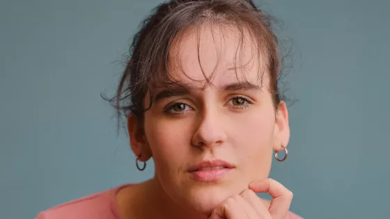 A young woman, Rebecca, looks thoughtfully beyond the character.