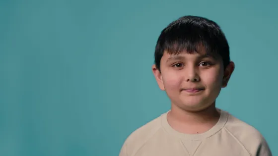 Young Asian boy smiles as he's talking, against a blue backdrop