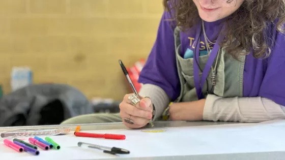 Young girl wearing a Purple Day t-shirt writing in a classroom