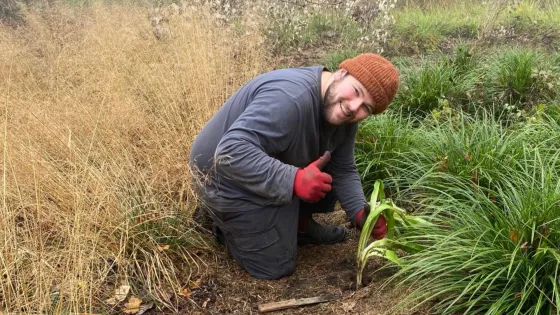 A young man smiles as he tends his garden.