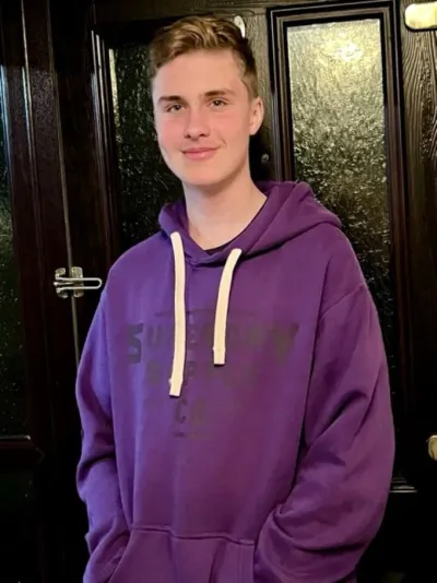 A teenager, wearing a purple hoodie, smiles at the camera.