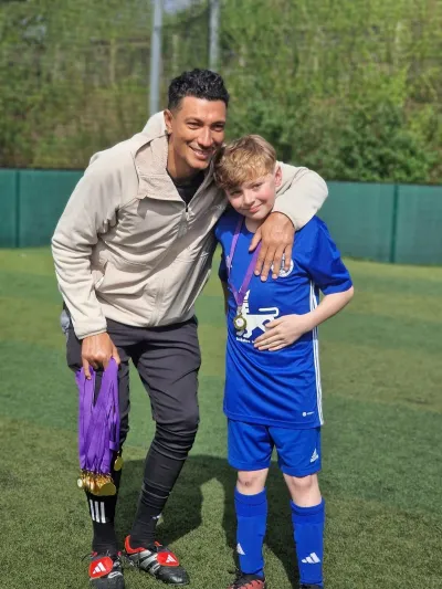 Footballer Jay Bothroyd smiles and poses with a child in a football kit.