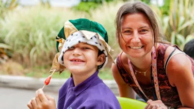 Young boy wearing a green velvet crown sat next to an adult woman. Both are smiling towards the viewer.