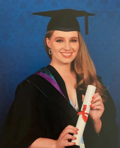 A young woman holds her degree and smiles in a graduation photo.