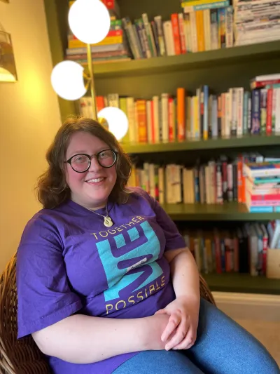 A young women in a Young Epilepsy shirt smiles by a bookcase.