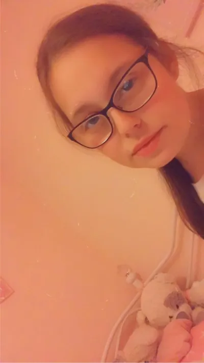 A young woman in glasses looks into the camera for a selfie.