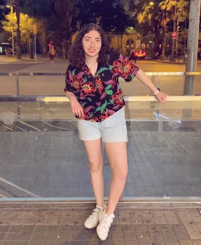 A young woman in a floral shirt smiles for a photo taken at night.
