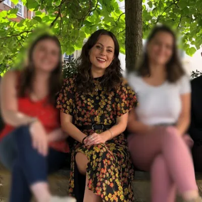 A smiling woman in a floral dress sits between two other women, whose faces are blurred.