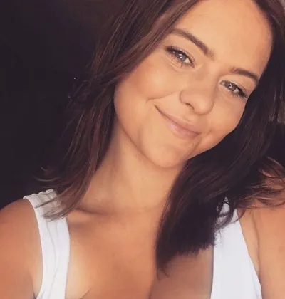 Jasmine, a young woman in white vest, smiles with her head tilted in a selfie.