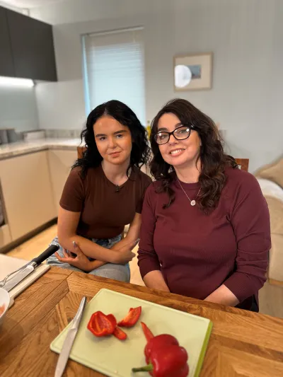 A mother and daughter sit at a kitchen table before a chopping board.