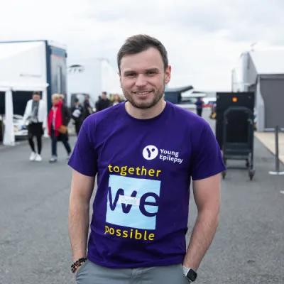 A young man wearing a Young Epilepsy shirt with the quote 'together we create possible' smiles for the camera.