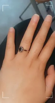 A woman's hand reveals an engagement ring with a black stone.