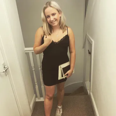 A girl in a black dress holds a notebook and smiles for a photo.