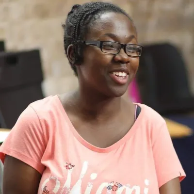A young woman wearing a pink t-shirt and glasses smiles off camera.