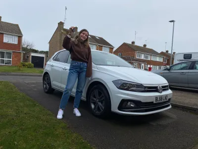 Young woman stands by a car and holds up her car keys.