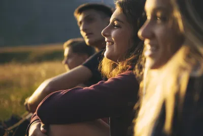 A group of teenagers sit smiling in a row outside in the low light of sunset.