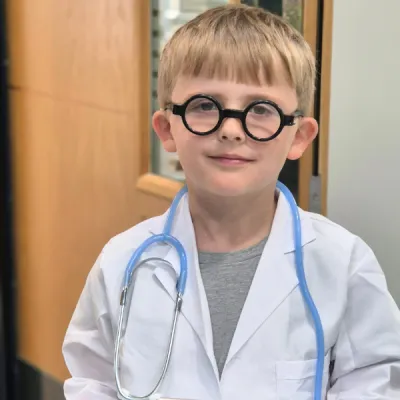 A child is wearing character glasses and stethoscope with a doctor's coat.