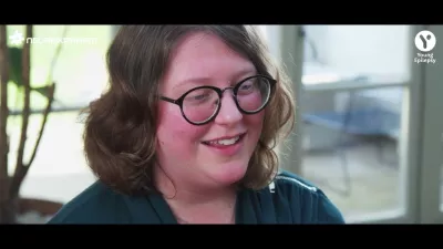 A young woman in glasses smiles off camera