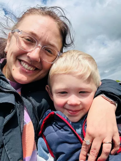 A woman in glasses smiles with her arm wrapped around her son.
