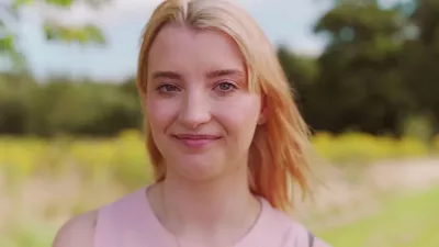 A young woman, Bethany, stands smiling outside, the background slightly blurred.