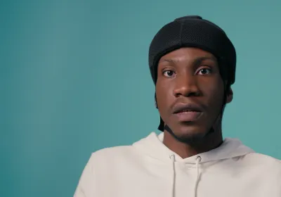 A young boy in a wheelchair with a protective helmet against a blue backdrop wearing a white t-shirt