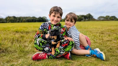 Two boys, Rafferty and Fin, sit in a field with a small dog.