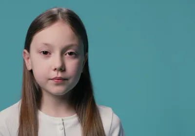 A young Caucasian girl stands against a blue backdrop wearing a white t-shirt