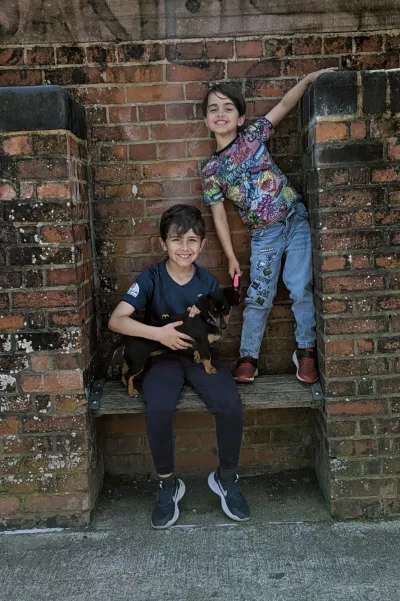 Two boys and a dog pose against a rustic brick wall.