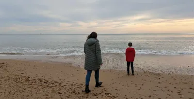 A mother approaches her son on a sunset beach.