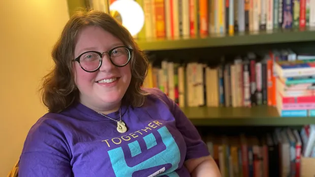 A young women in a Young Epilepsy shirt smiles by a bookcase.