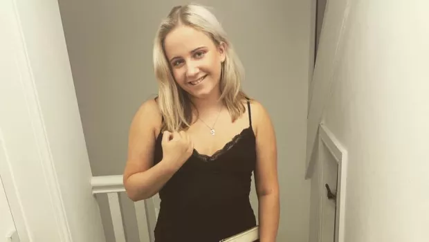 A girl in a black dress holds a notebook and smiles for a photo.