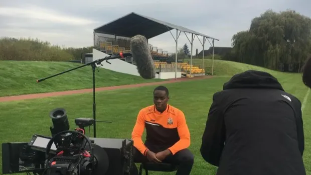 A young man sits before film cameras on a football pitch for a Christmas appeal.