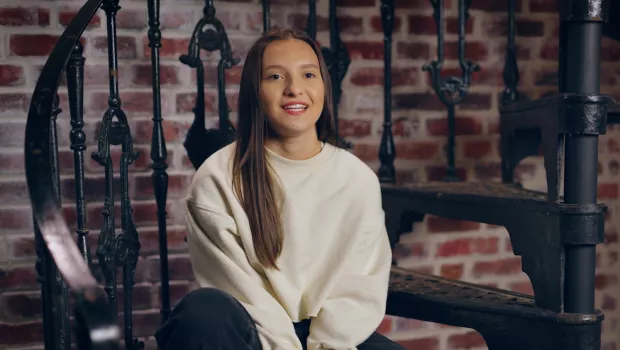 young girl sat talking to camera on some stairs