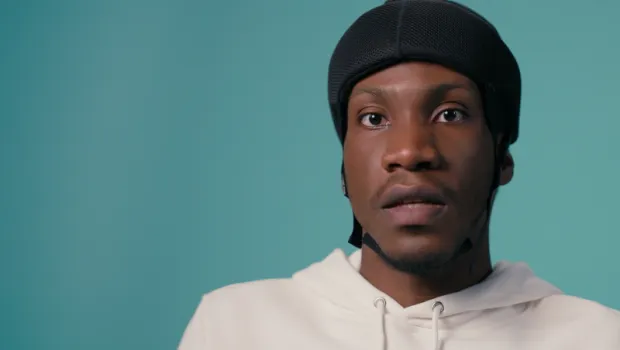 A young boy in a wheelchair with a protective helmet against a blue backdrop wearing a white t-shirt