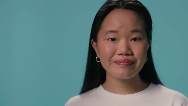 A young Asian girl stands against a blue backdrop wearing a white t-shirt