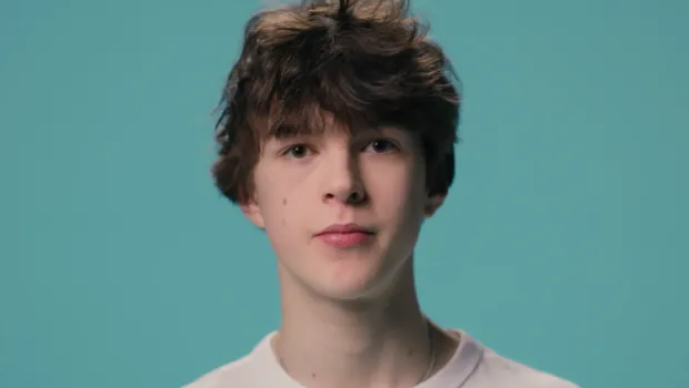A young boy stands against a blue backdrop wearing a white t-shirt