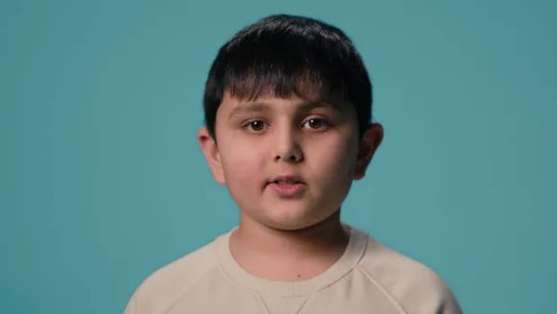 A young Asian boy stands against a blue backdrop wearing a white t-shirt