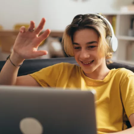 A teenage boy smiles and waves on a video call.