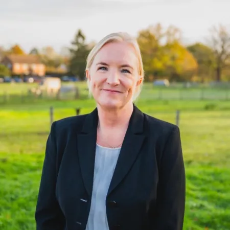 Jane Beaven smiles against a background of green foliage.